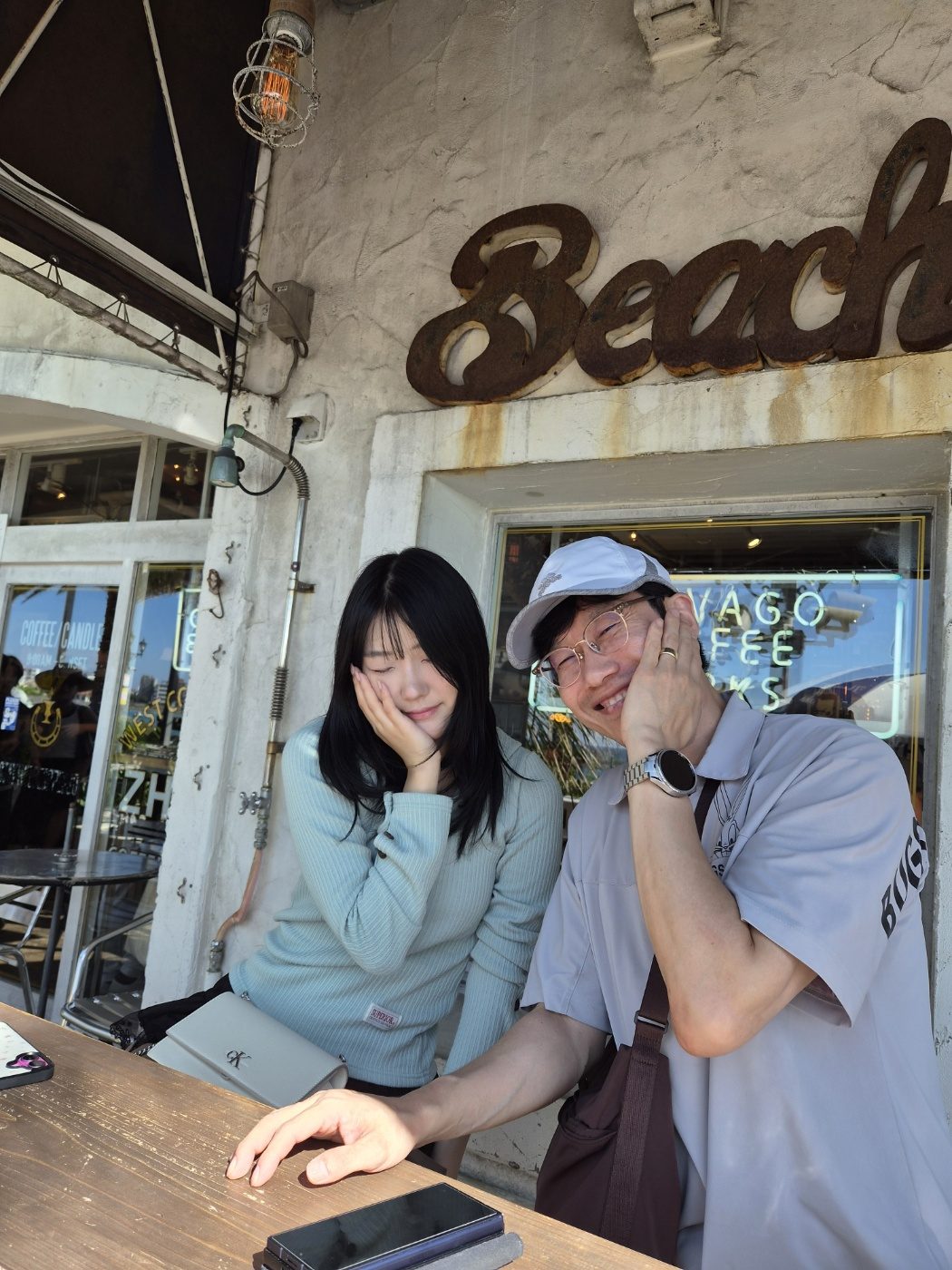 Beach 간판 아래 테이블에 앉은 딸과 아빠