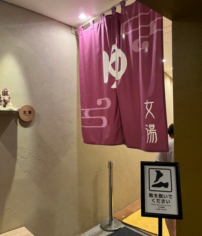 ゆ 글자와 女湯이 적힌 자줏빛 노렌이 걸린 대욕장 입구